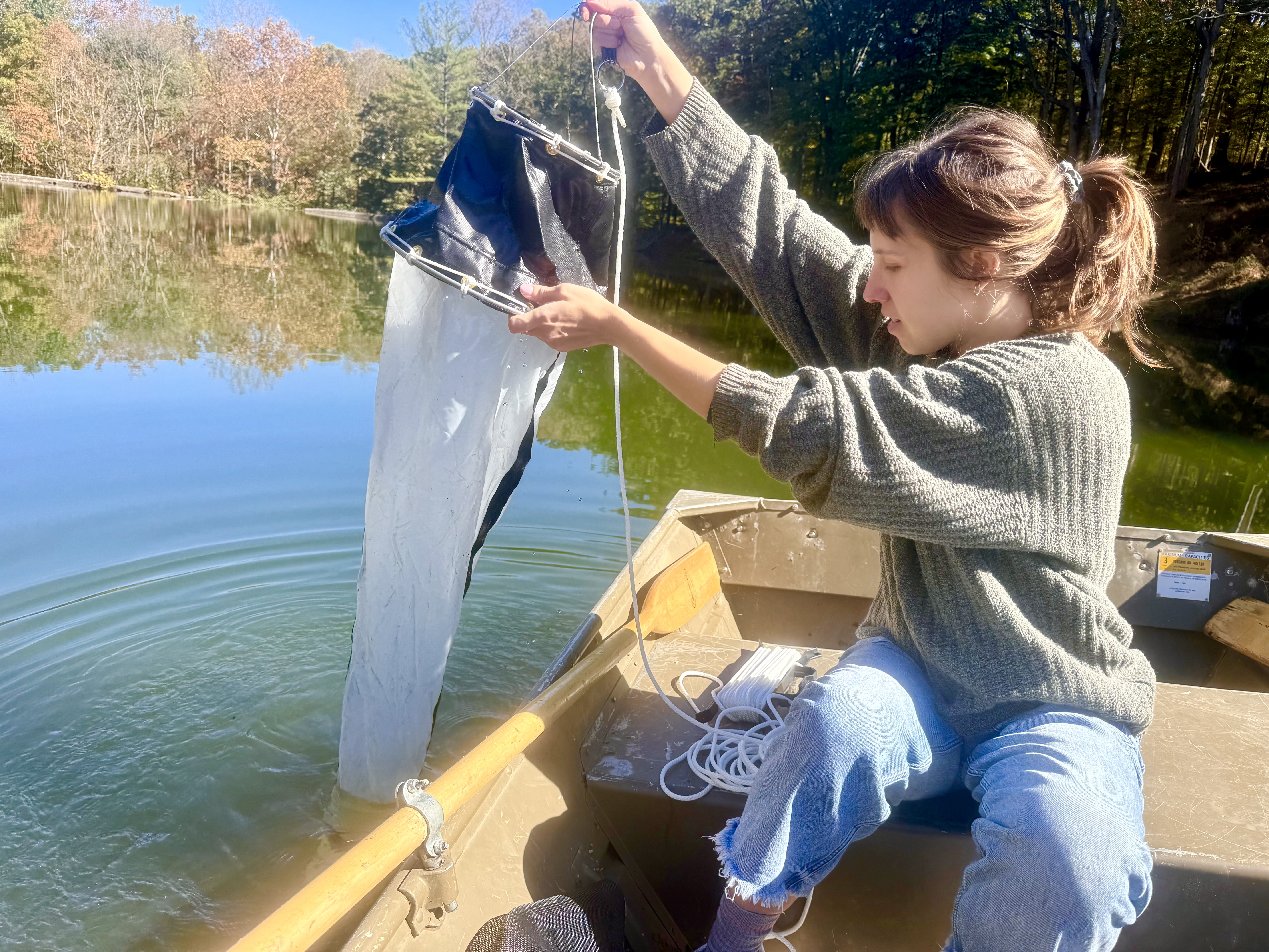 A person, reeling in net from boat on lake